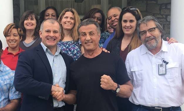 A photo of Sylvester Stallone with a group of people, shaking hands with one of them