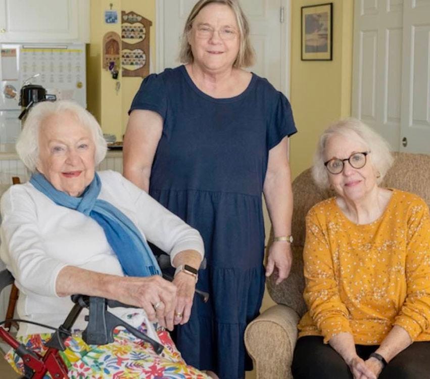 Three older white women visit in a pleasant yellow room.