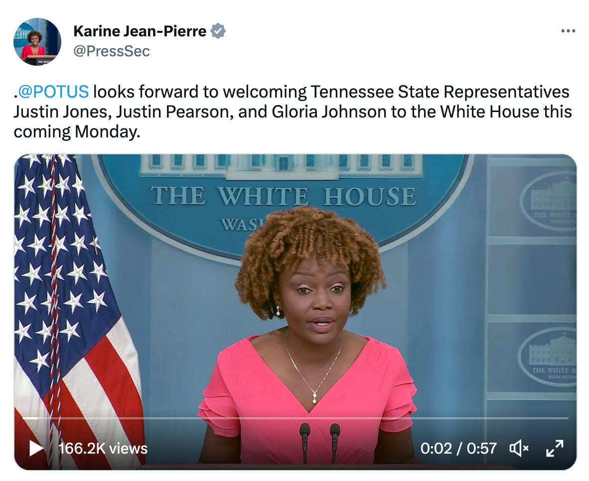 A screenshot of a tweet from Press Secretary Karine Jean-Pierre speaking at the podium in the press room wearing pink.