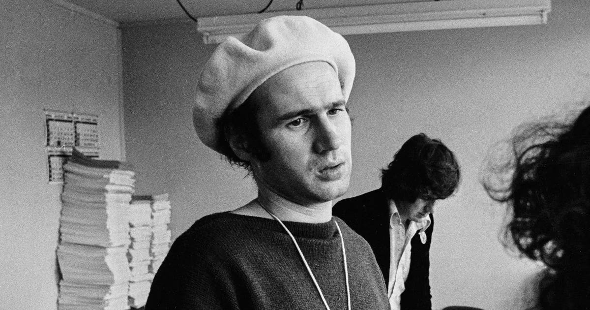 A man in a hat in front of a stack of scripts