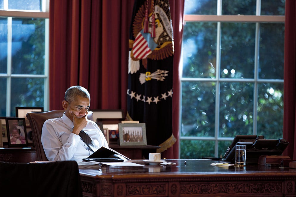 This image shows an undated photo of President Barack Obama sitting at the Oval Office's Resolute Desk while reading a briefing book. Obama holds his right hand over his mouth while looking down at his briefing book. This image shows an undated photo of President Barack Obama sitting at the Oval Office's Resolute Desk while reading a briefing book. Obama holds his right hand over his mouth while looking down at his briefing book.