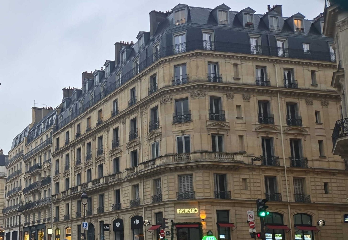 Image of a 7 story classical Parisian building with commerce on the ground level and top two levels appearing as a mansard roof.