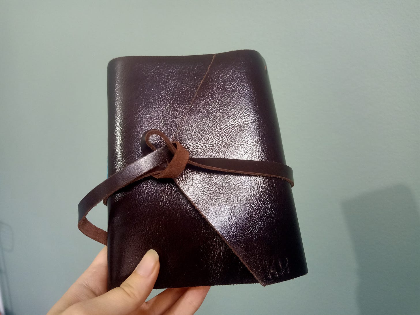 a brown leather journal held up with my hand against the teal blue/green wall in my office.