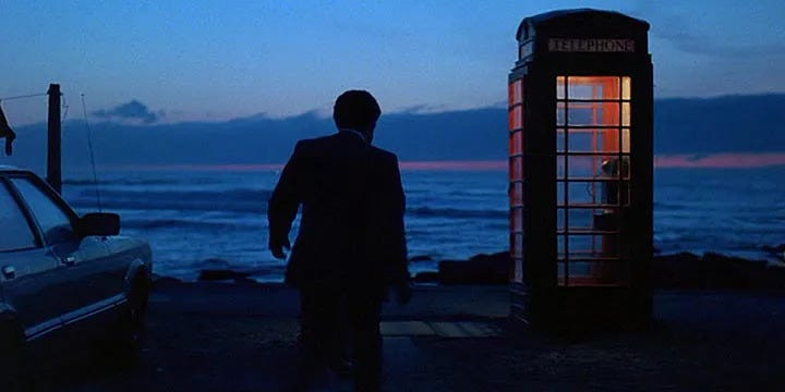 A man walks toward a phone booth on a pier in Scotland at dusk.