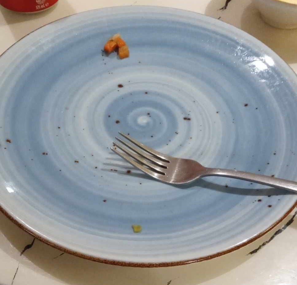 Image of a fork sitting on a blue plate. A few small pieces of carrot are on one side of the plate, but the plate is otherwise empty.