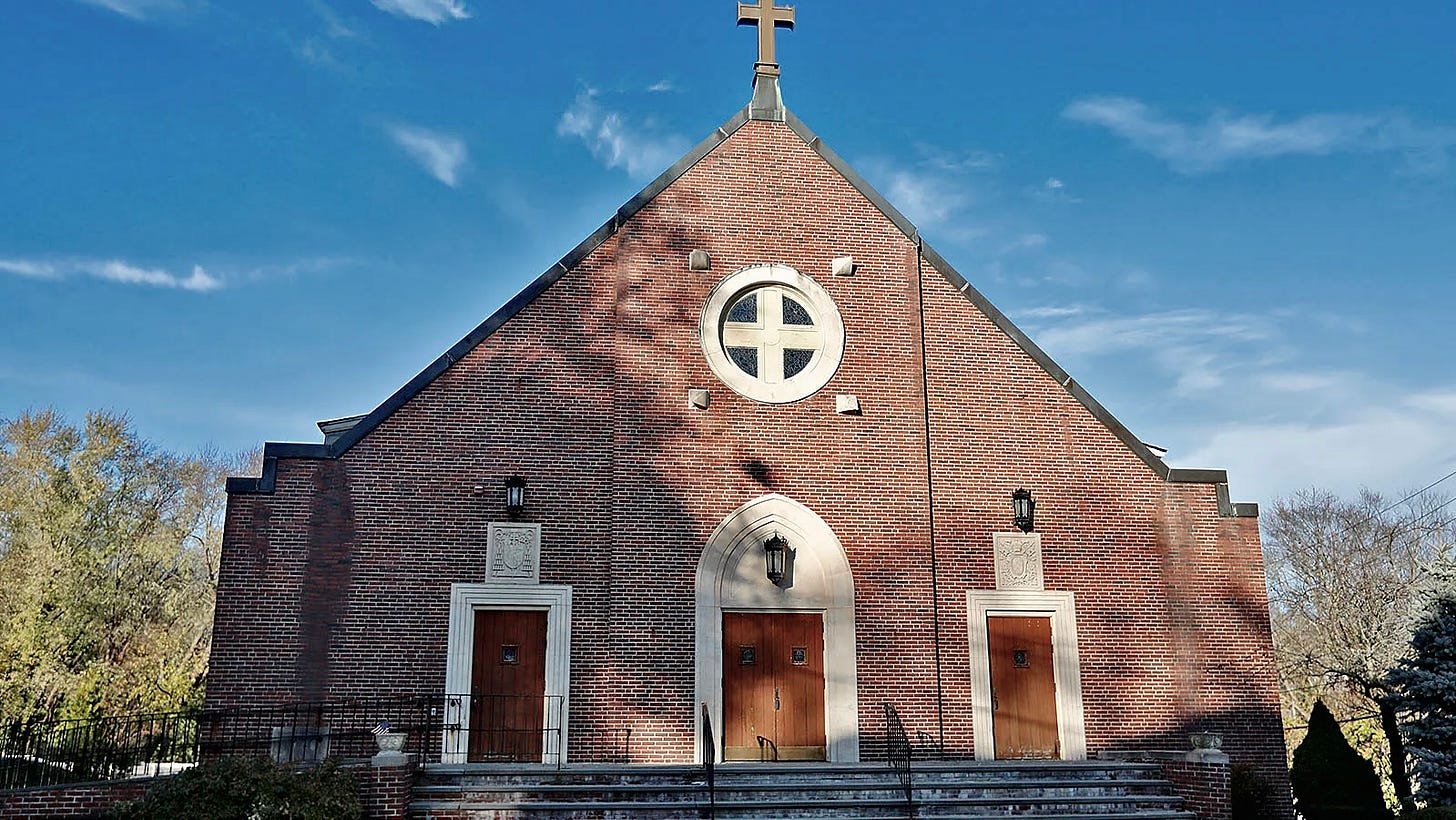 A brick church with a cross on top and blue sky.