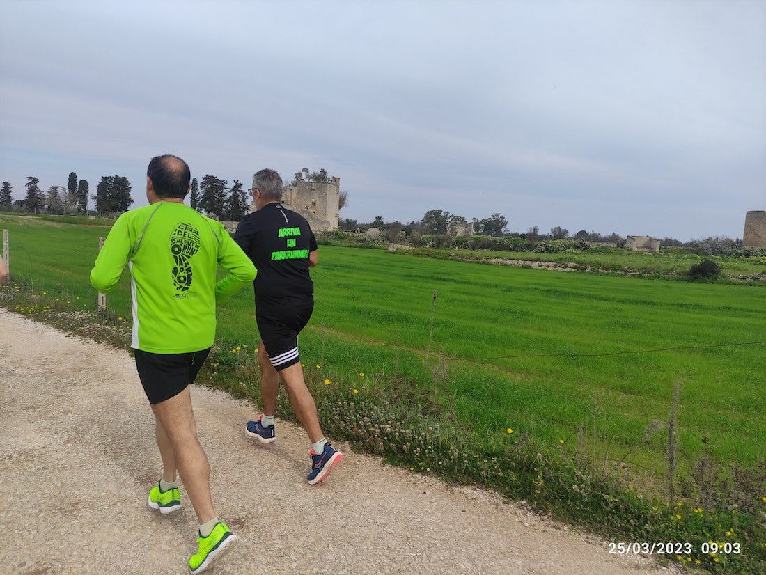 Two runners on the course, with the fortified farmhouse landmark in the distance