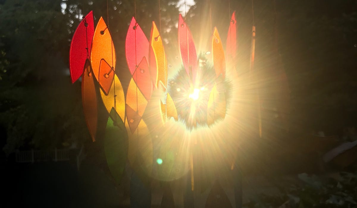 the sun shining through a rainbow glass wind chime made of many small frosted glass petals in different colors of the rainbow.