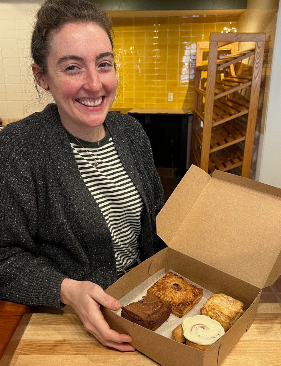A person smiling next to a box of donuts

Description automatically generated with medium confidence