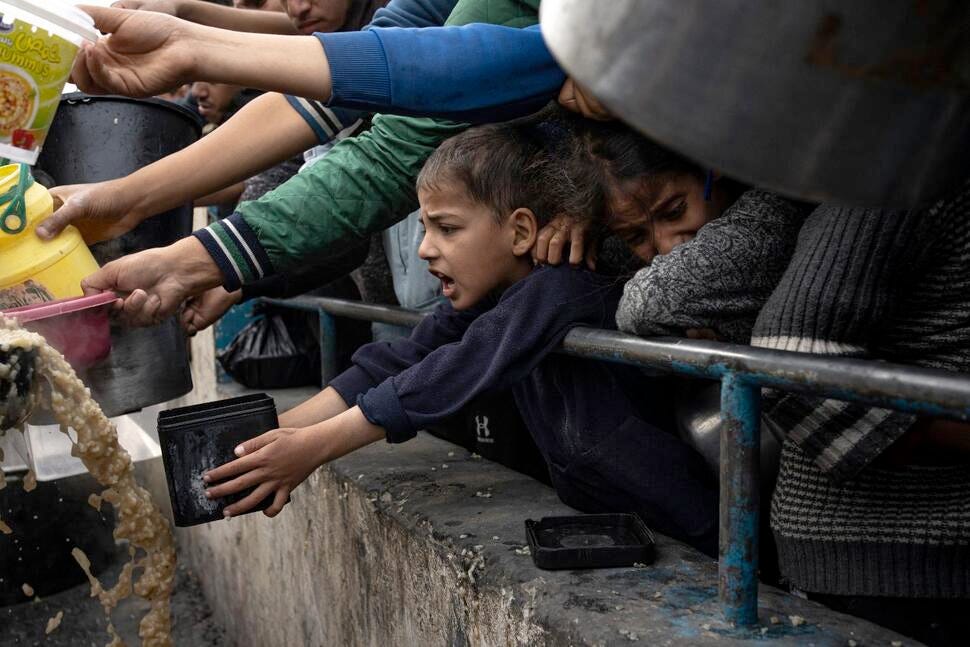 An anguished little boy reaches out with a container desperate for food, his exhausted mother on his shoulder.
