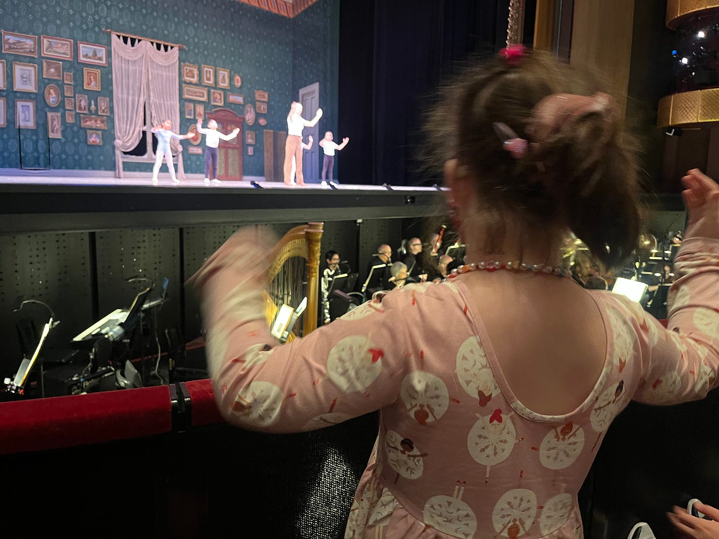 a six-year-old girl in a pink ballerina dress dancing in front of the orchestra pit at the New York State Theater
