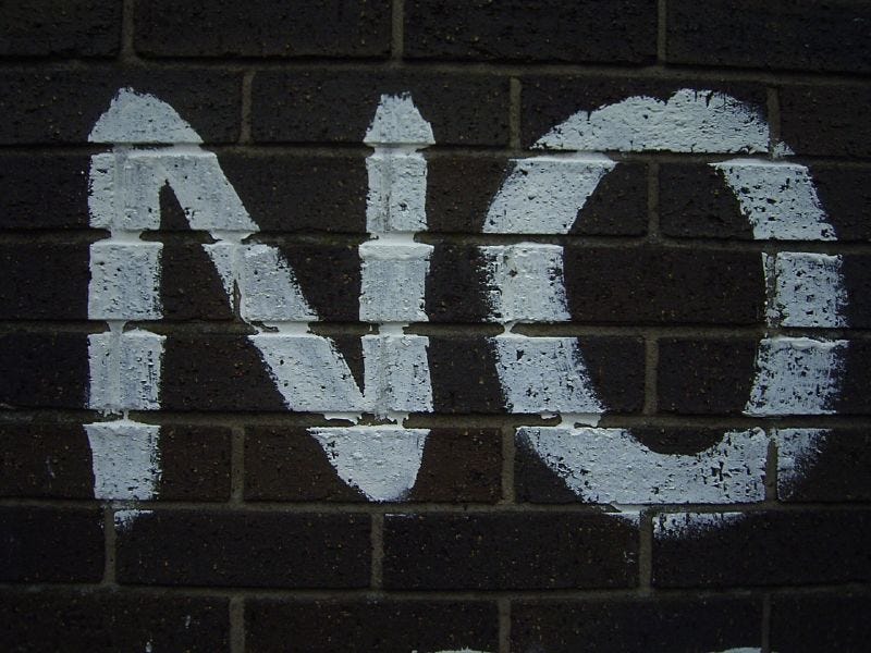 The word NO spray painted in white on a black brick wall. The word NO spray painted in white on a black brick wall.