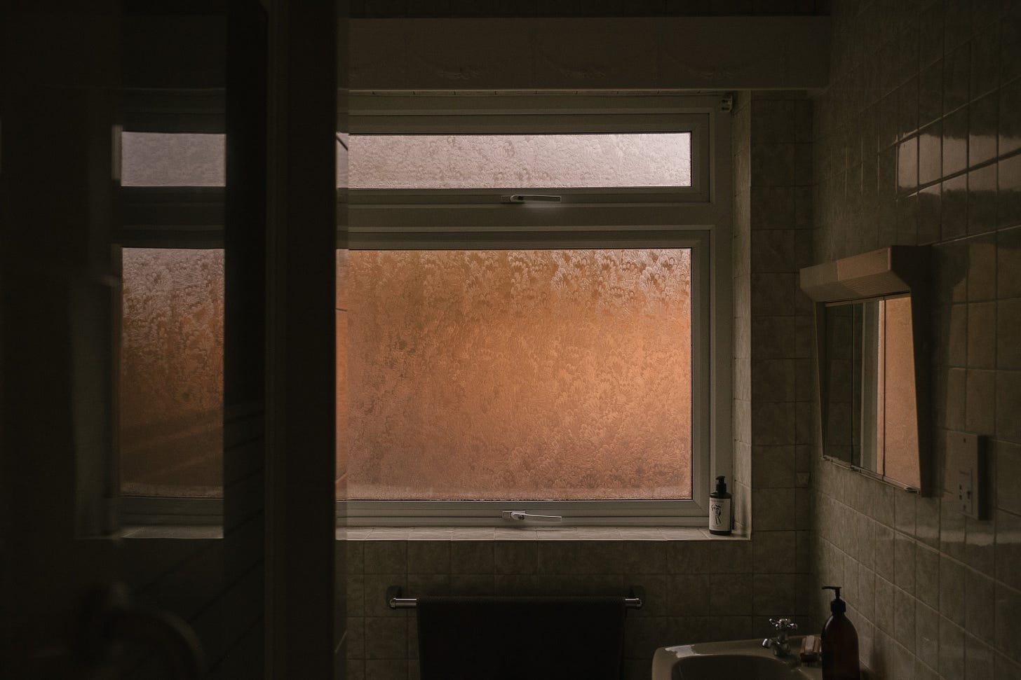 Looking into a bathroom towards the window in the glowing amber of early morning.