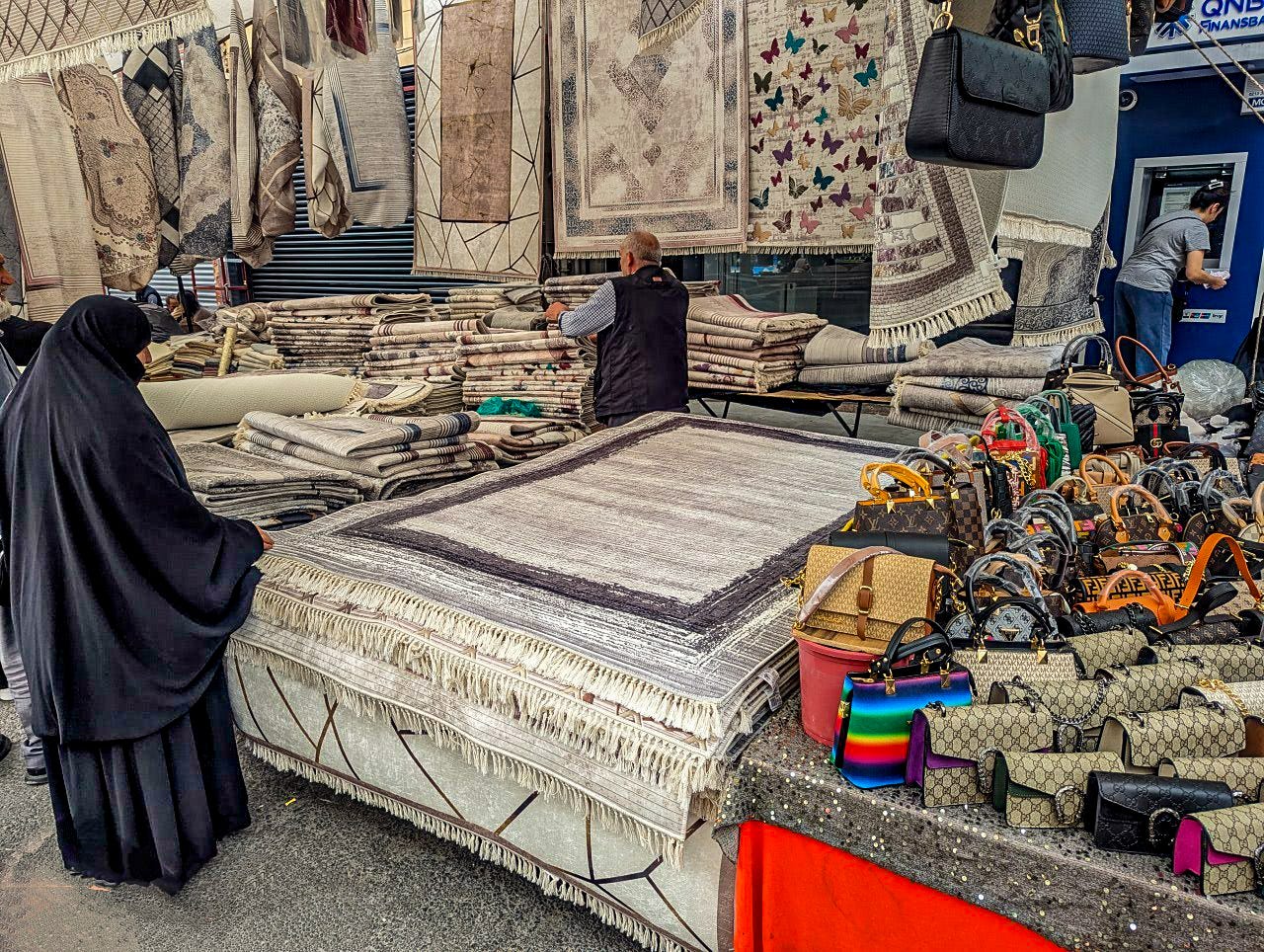 A woman dressed in a traditional black abaya looks at rugs.