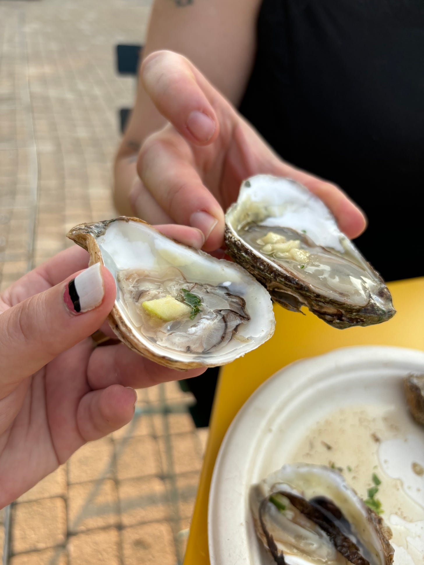 Two hands holding oysters on the half-shell toast as if there oysters were cocktails.