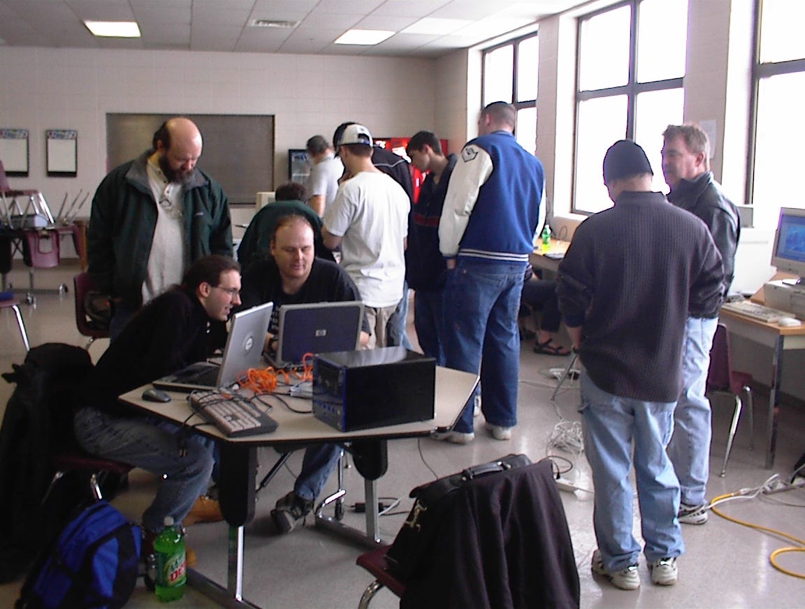 Several guys with computers installing software and/or socializing.