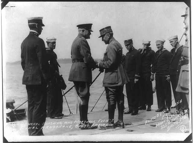 General Pershing shaking hands with Marshall Foch in Brest, France. Black and white photo on a ship with other soldiers looking on for the last meeting between Pershing and Foch at the end of World War I.