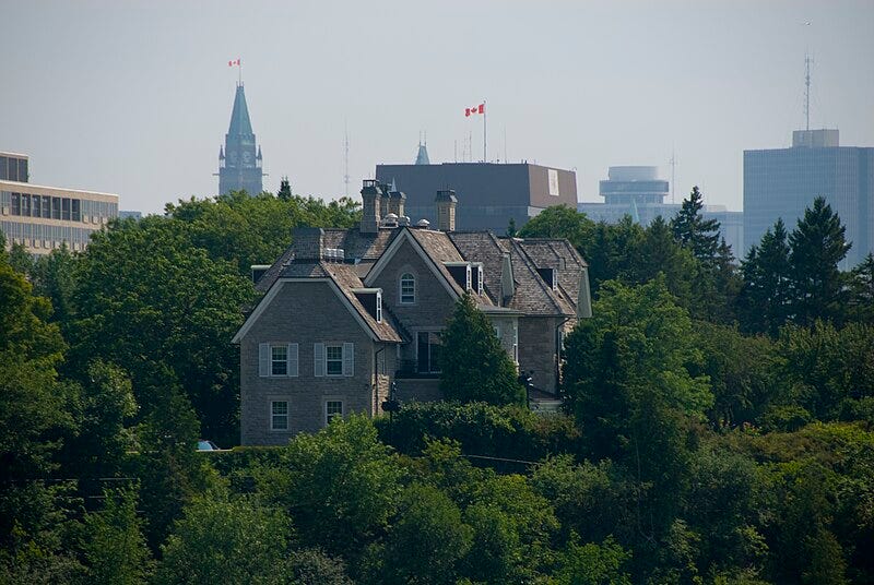 24 Sussex, the official residence of Canada's prime minister, pictured against a backdrop of trees, with the Parliament buildings in the background.