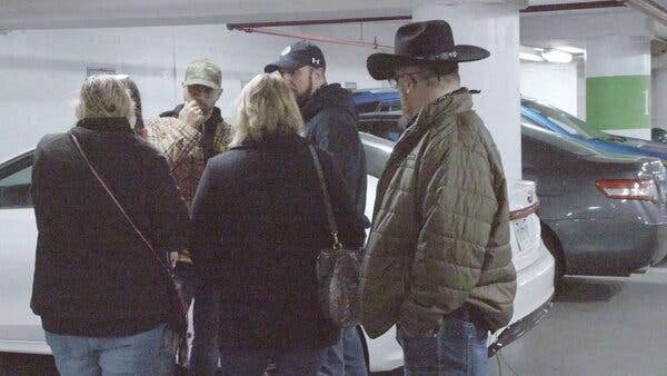 A small group of people standing near cars in a garage.