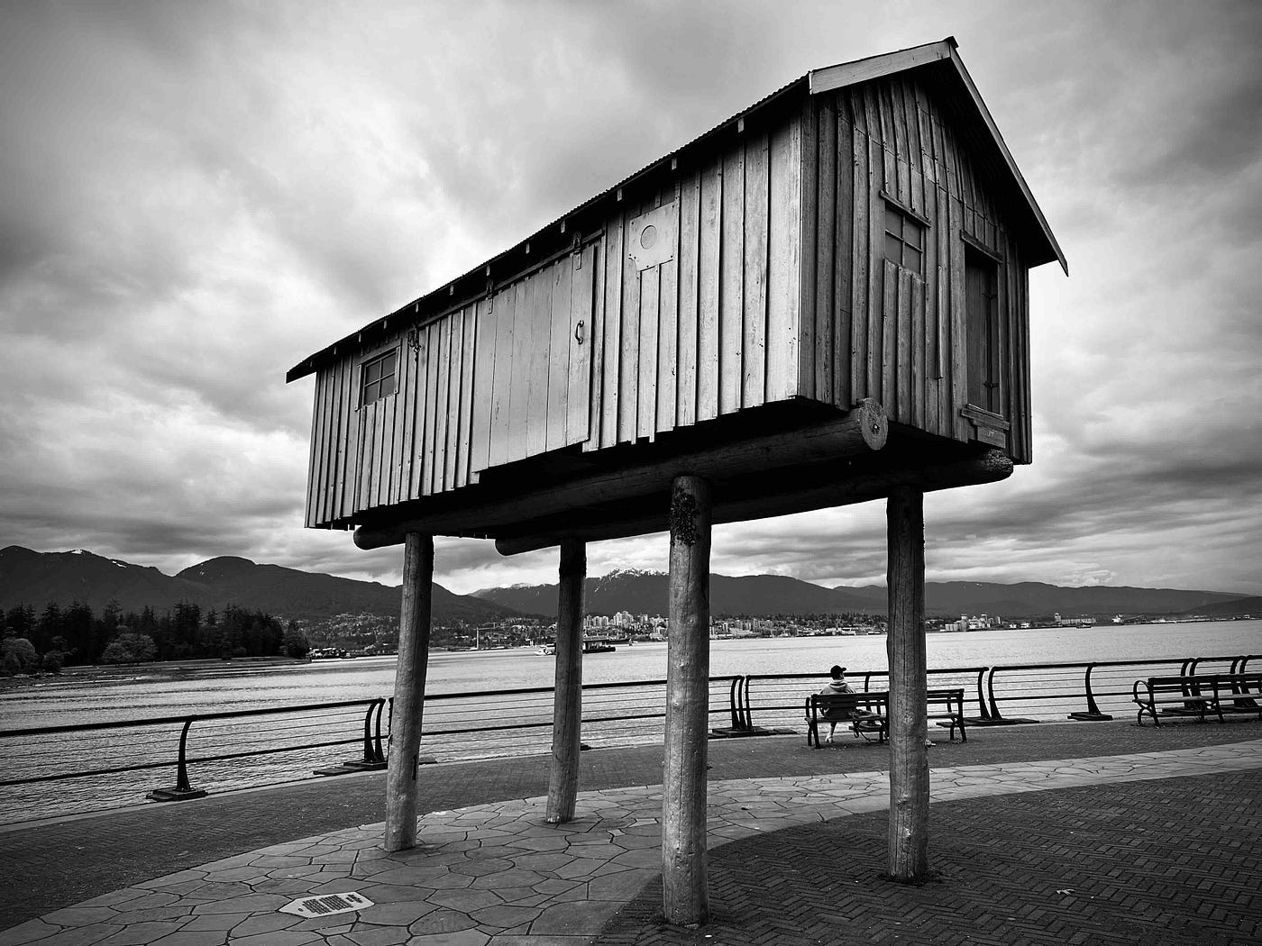 House on stilts against mountain and ocean backdrop. Black and white photograph.