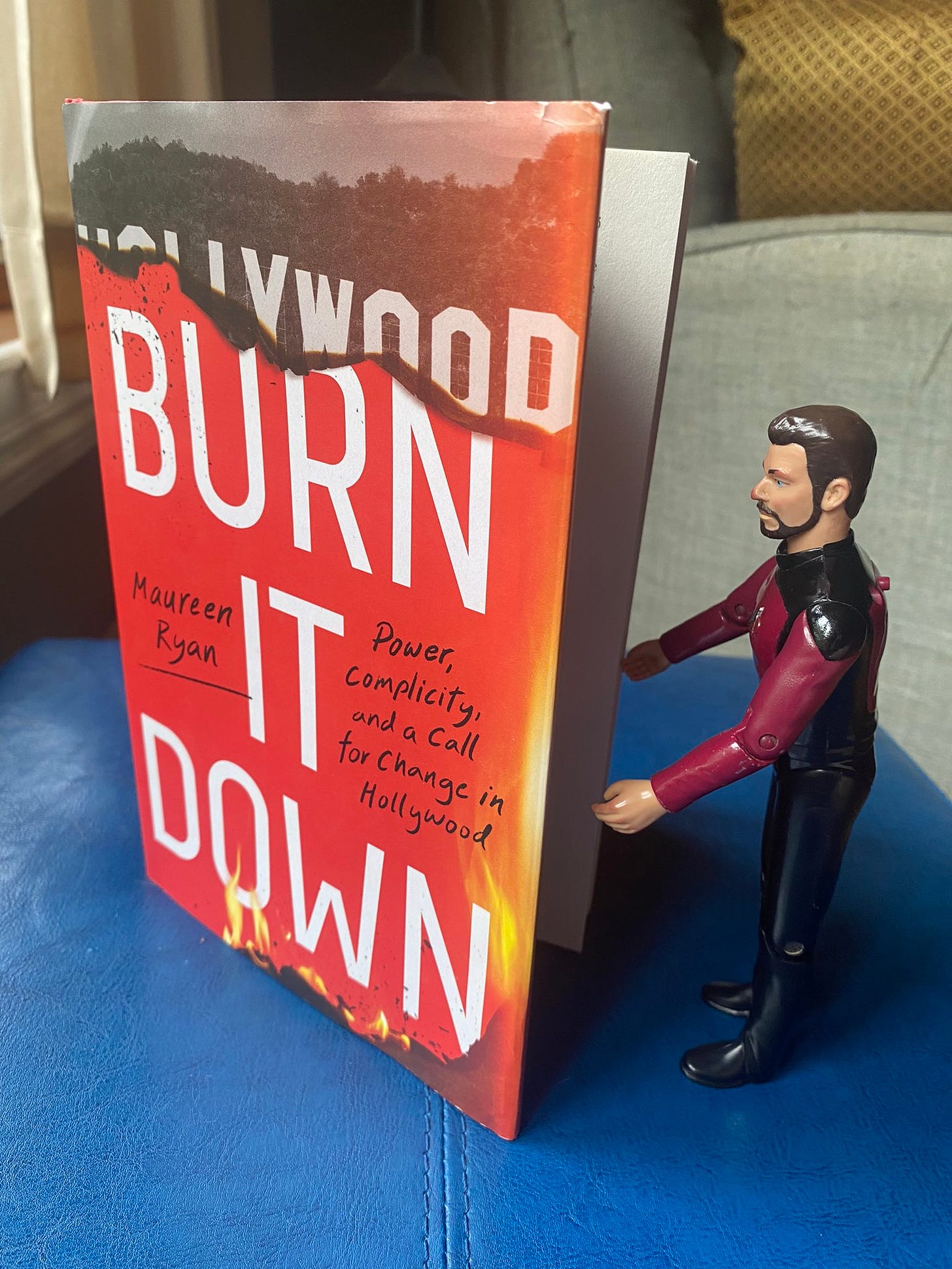 Little Riker action figure with the book Burn It Down by Maureen Ryan