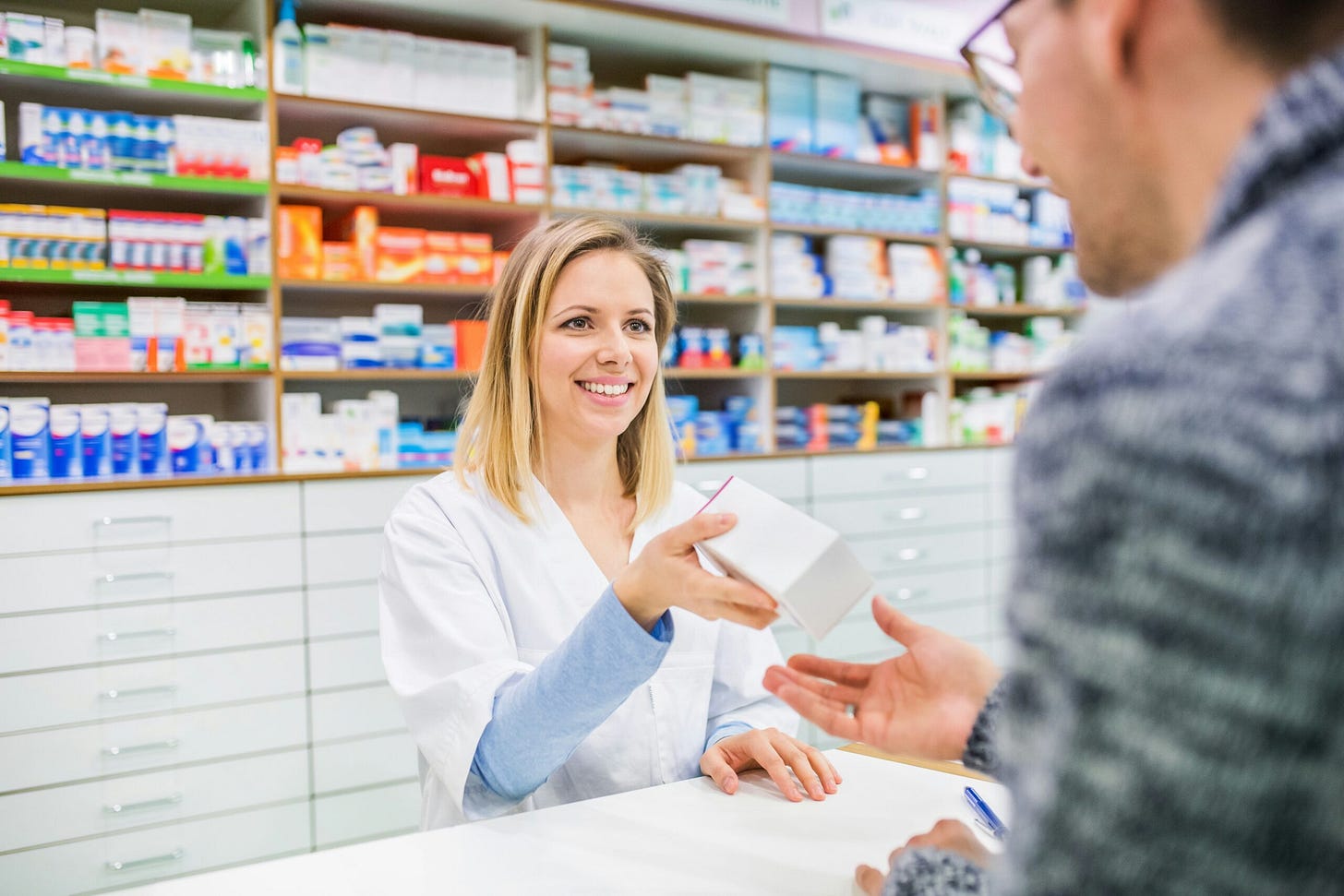 A young pharmacist smiles as she gives a patient a box of medicine