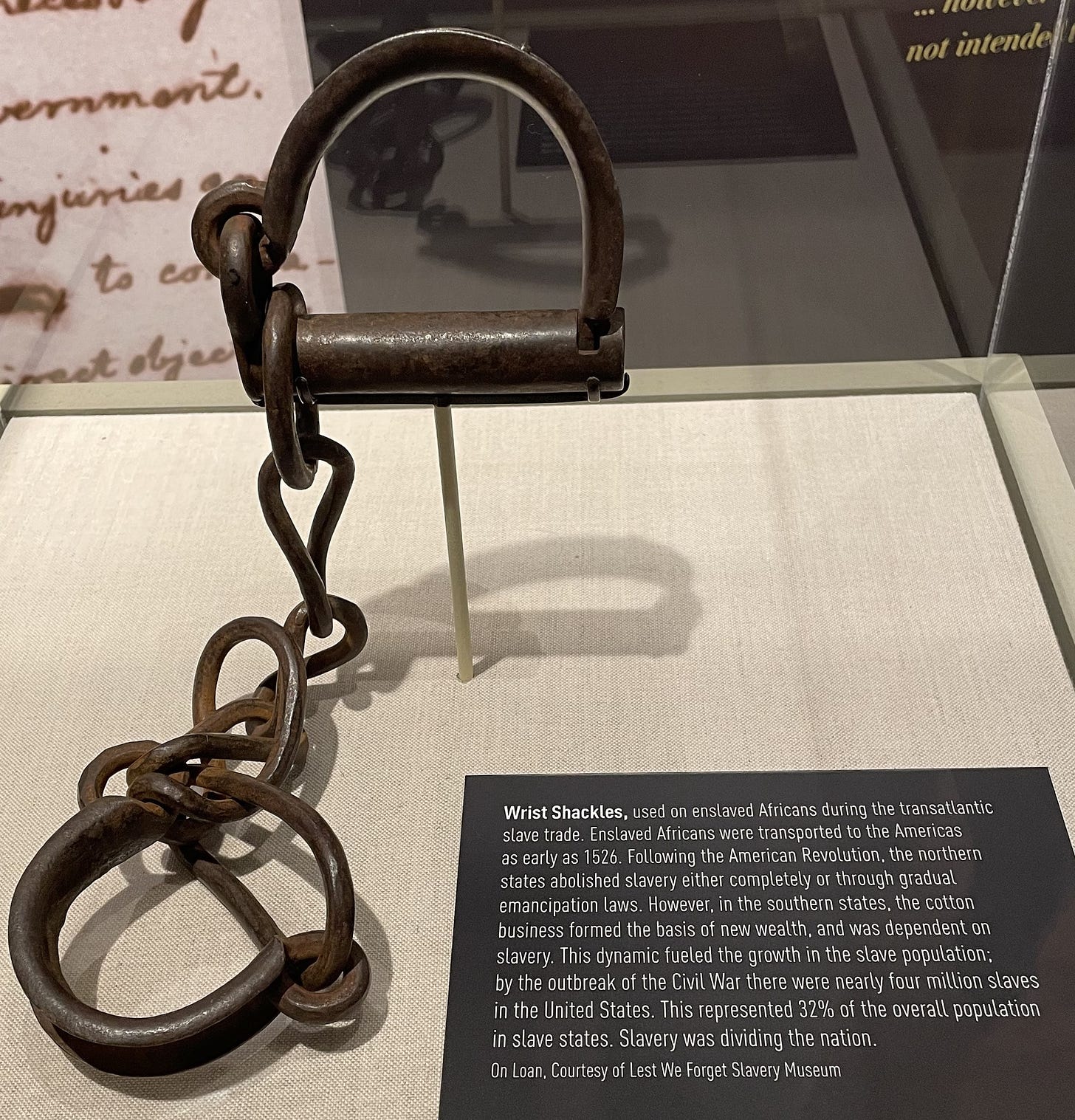 Iron wrist shackles in display case with accompanying museum label.