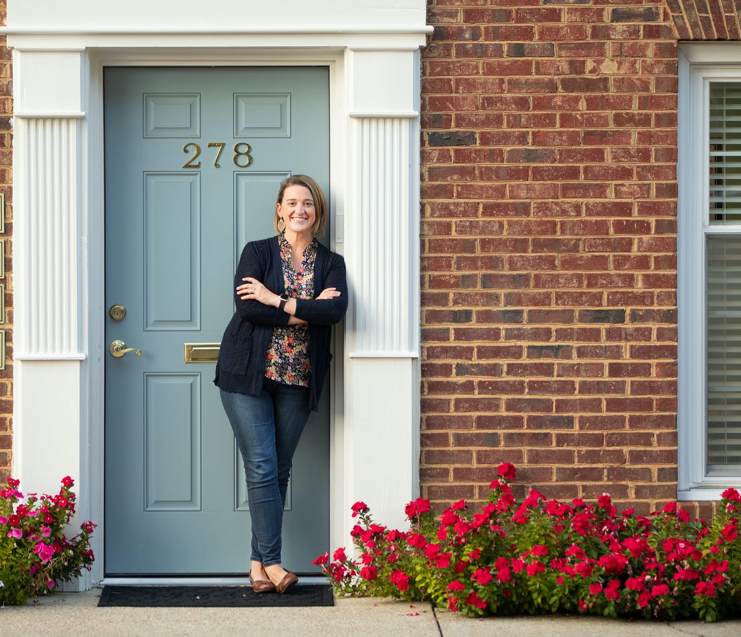 Dr. Emily standing outside her office smiling in front of a light blue door and pink flowers