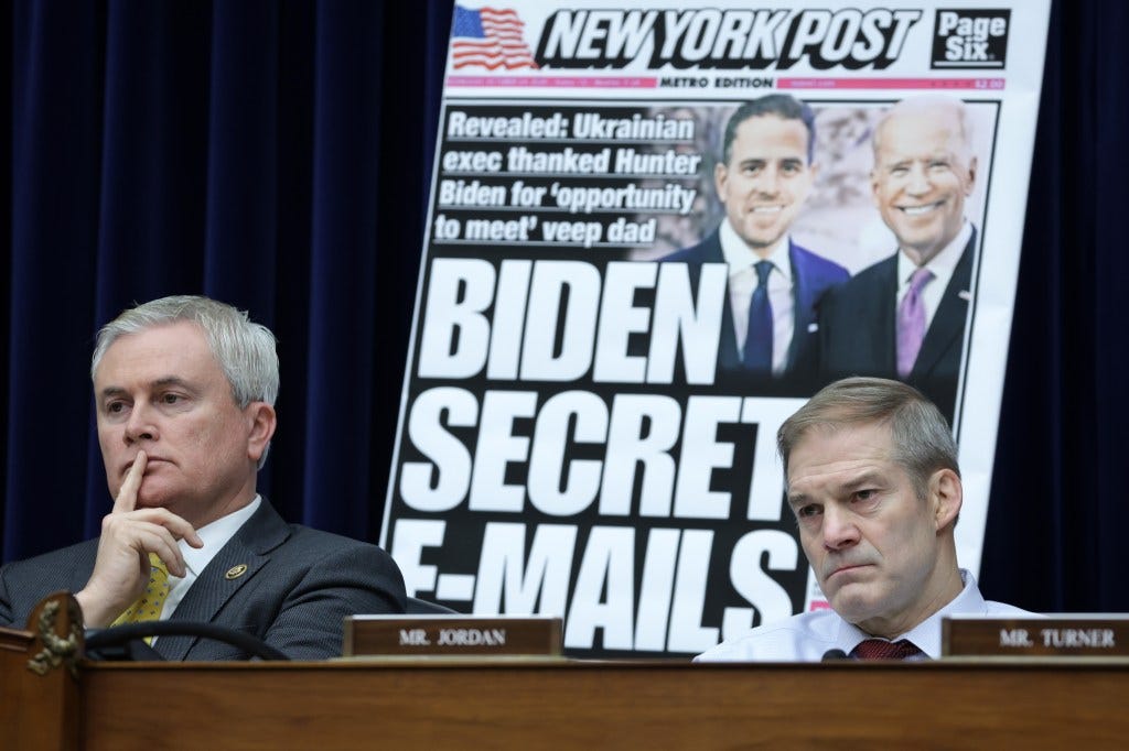 Two men sit at a hearing podium with a poster of a newspaper headline that reads "Hunter Biden's emails".