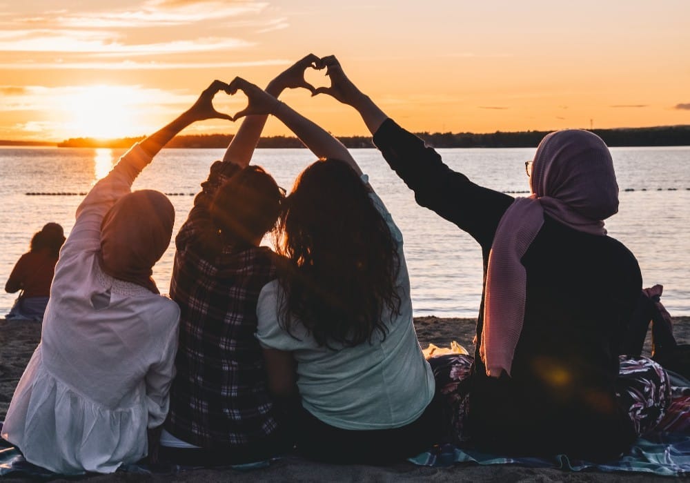 Group of friends on the beach making hearts with their hands at sunset