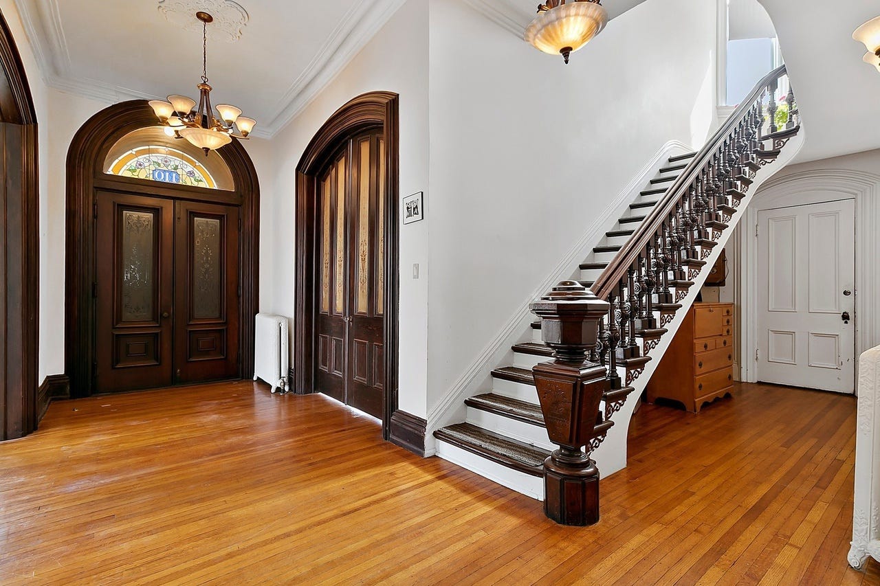 Entryway of Victorian home. To the left are walnut double doors with a colorful transom window above. To the right is a grand staircase.