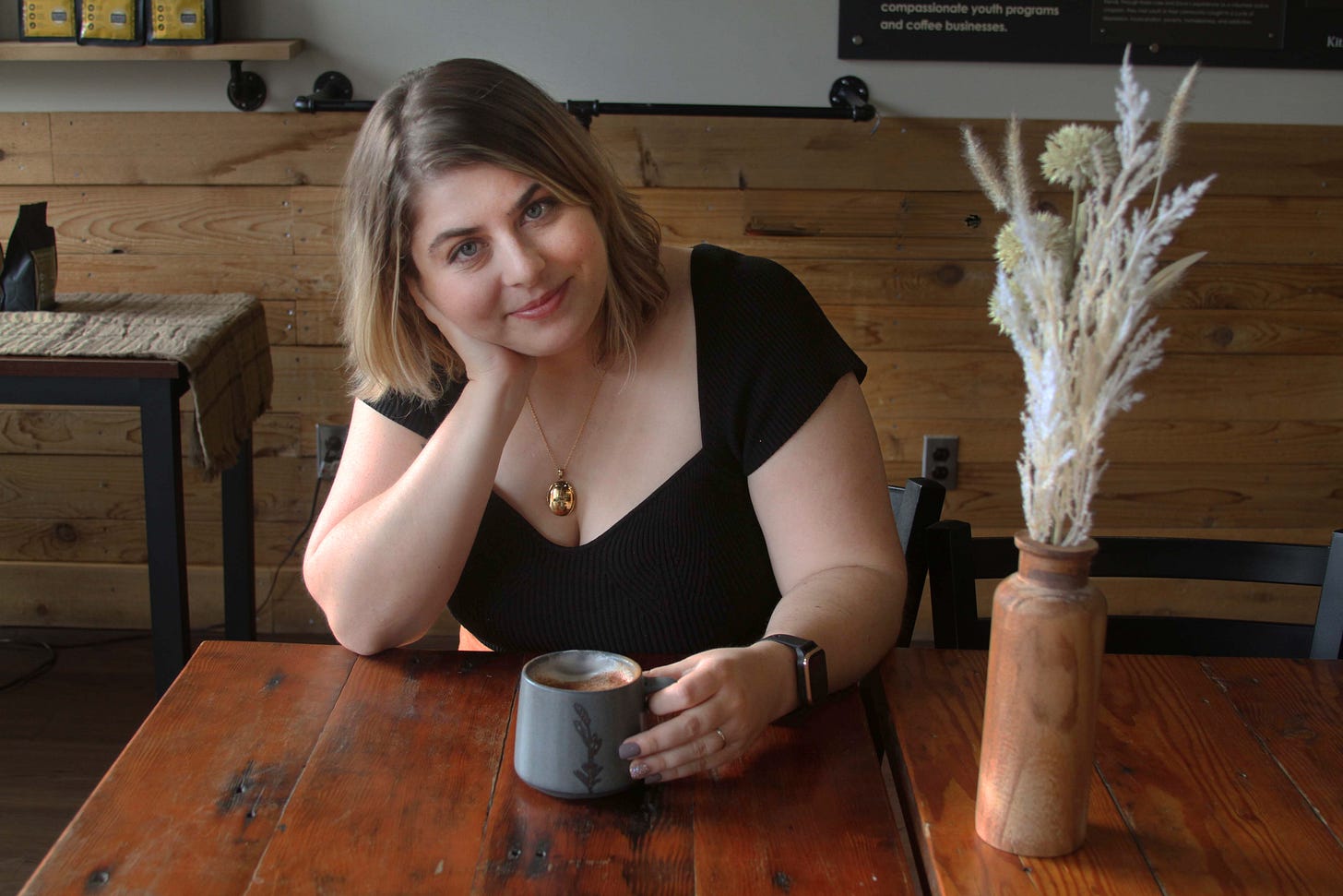 Portrait of Chanel wearing a black shirt and sitting at a table with a coffee mug in her hand.