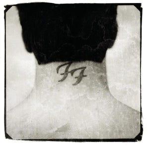 Black and white photograph of the back of Dave Grohl's head. A tattoo of the Foo Fighters logo is seen on his neck.