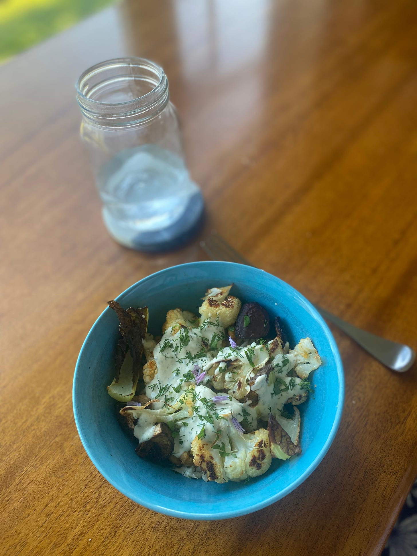 A blue bowl of the roasted vegetable rice bowl described above, covered with tahini ranch and chopped dill and parsley, and a few chive blossoms. 