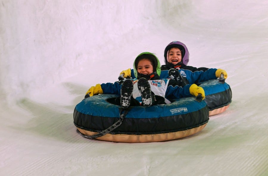 Two children sled down an indoor snow slope in inner tubes.