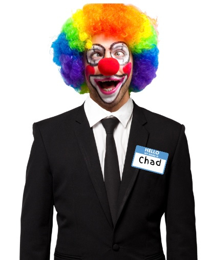 The head and torso of a man in a black business suit facing forward. The man has on thick clown make up and a rainbow wig. He has a maniacal smile. There is a name tag on his left breast pocket that reads, “Hello, my name is…” and the word “Chad” in written in the blank space.