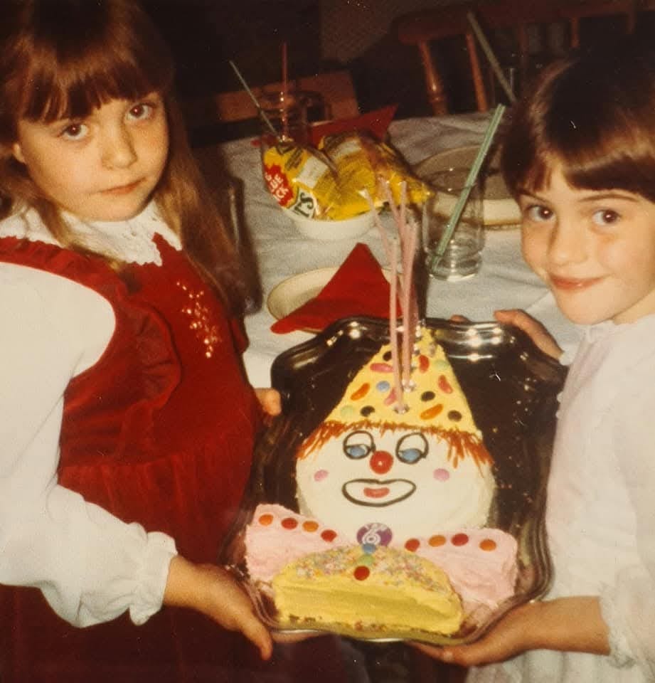 Two children holding a birthday cake in the shape of a clown made by their parents