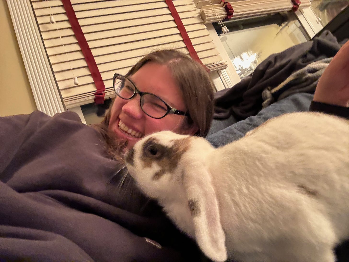Me (a white woman in a Black sweatshirt) with a white lop rabbit with brown splotches licking her