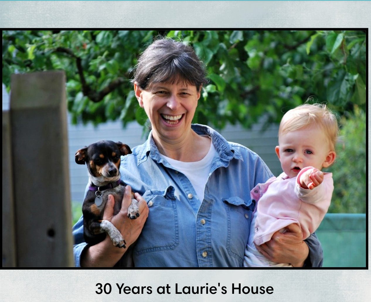 Photo of Laurie carrying our dog Liza in one arm and a toddler in the other. She has a big smile.