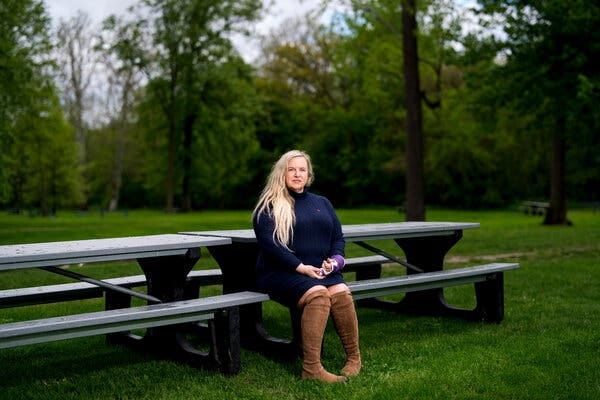 Jennifer Wright, wearing a blue dress, brown knee-high boots and a white cast on her wrist, sits at a picnic table in a park. 