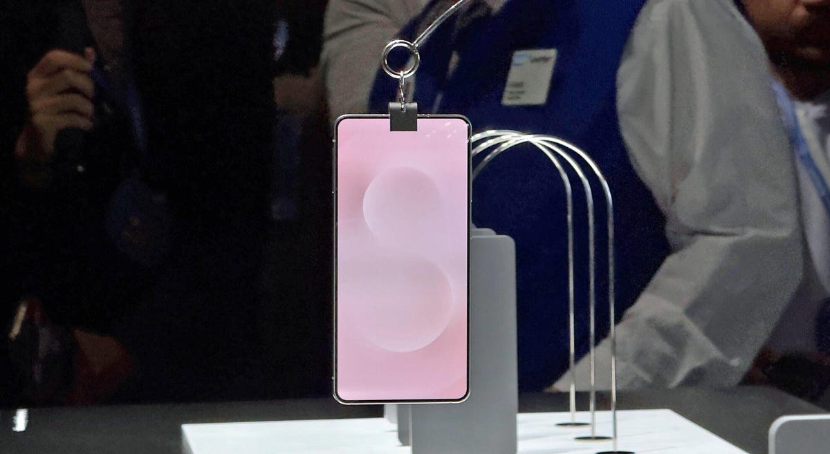 A phone with a pink screen background hangs from a clip on a display floor.
