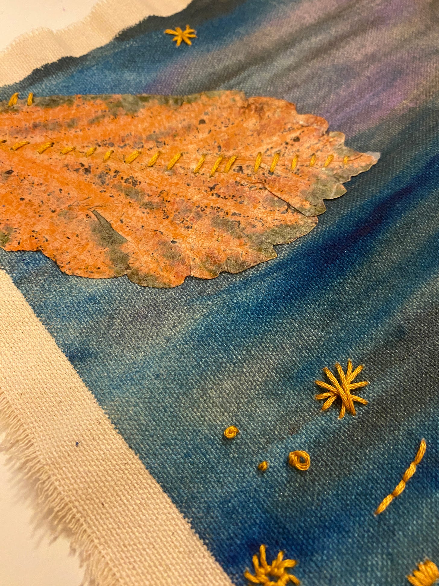 painted canva with an autoumn leaf and some rudimentary embroidery stitches