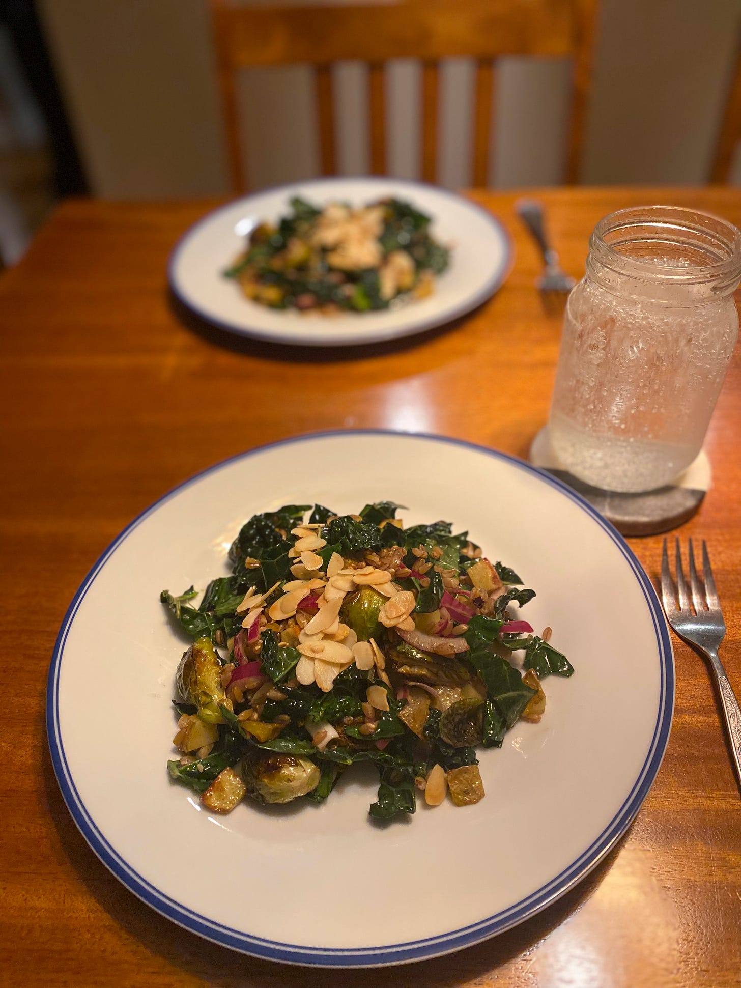 Two large plates of the salad described above, with toasted nuts and pickled red onion on top. A glass of sparkling water rests on a coaster above the plate in the foreground.
