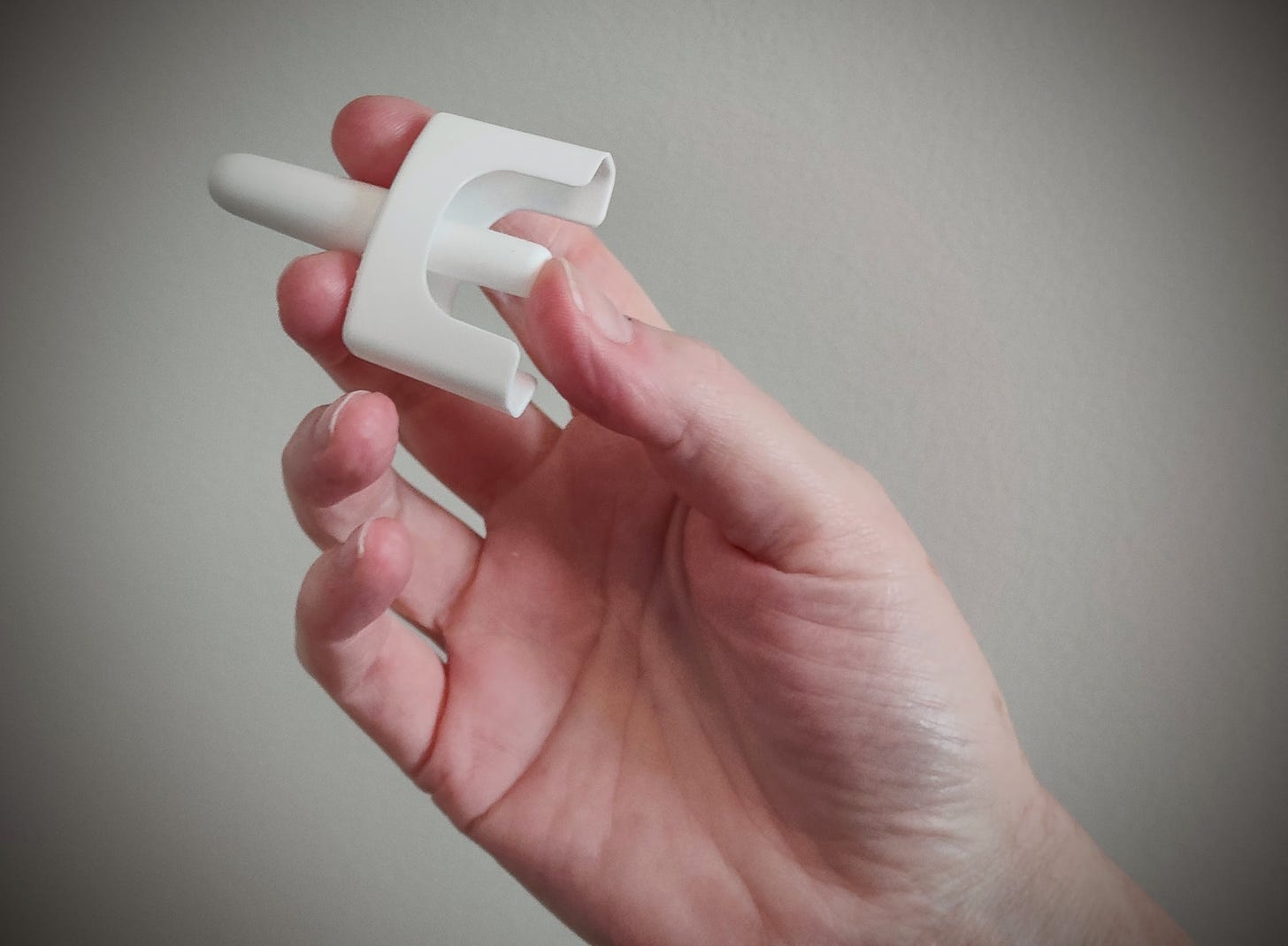 A hand holding a white nasal spray injector device against a grey background.