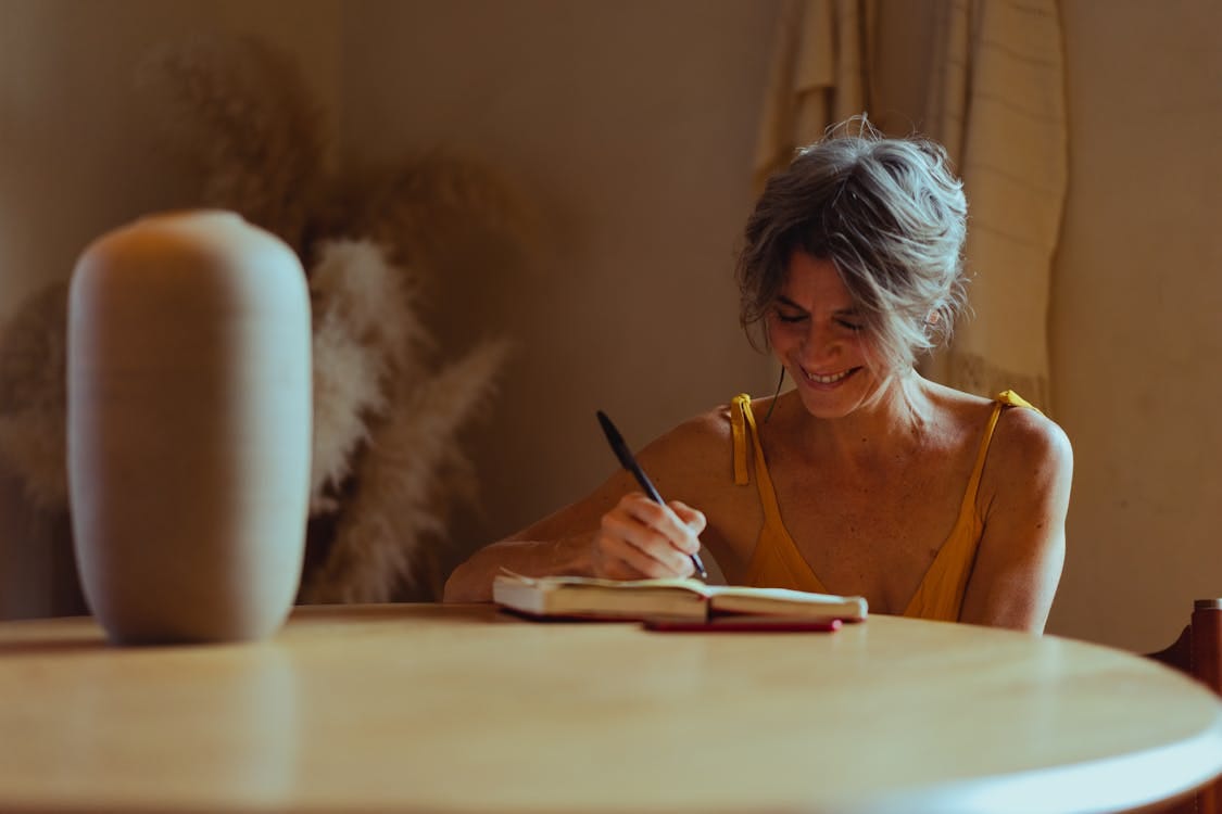 Free A senior woman sitting at a table, journaling happily in her cozy home office. Stock Photo