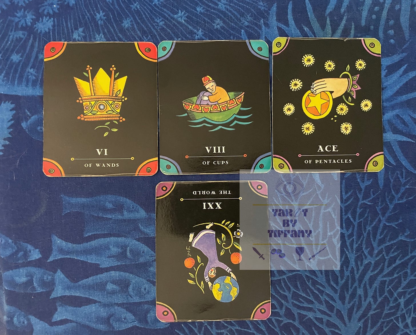 4-card reading using the Tarot Nova. The cards are laid against a blue cloth background with an aquatic motif in light blue. Top three cards (left to right): 6 of Wands, 8 of Cups, Ace of Pentacles. Bottom card: XXI-The World reversed.