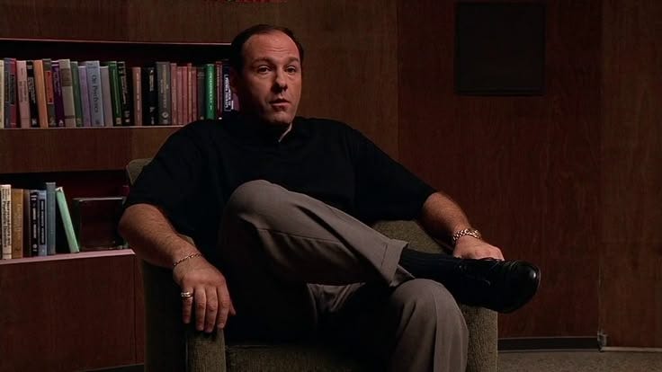 This may contain: a man sitting in a chair next to a book shelf with books on the shelves