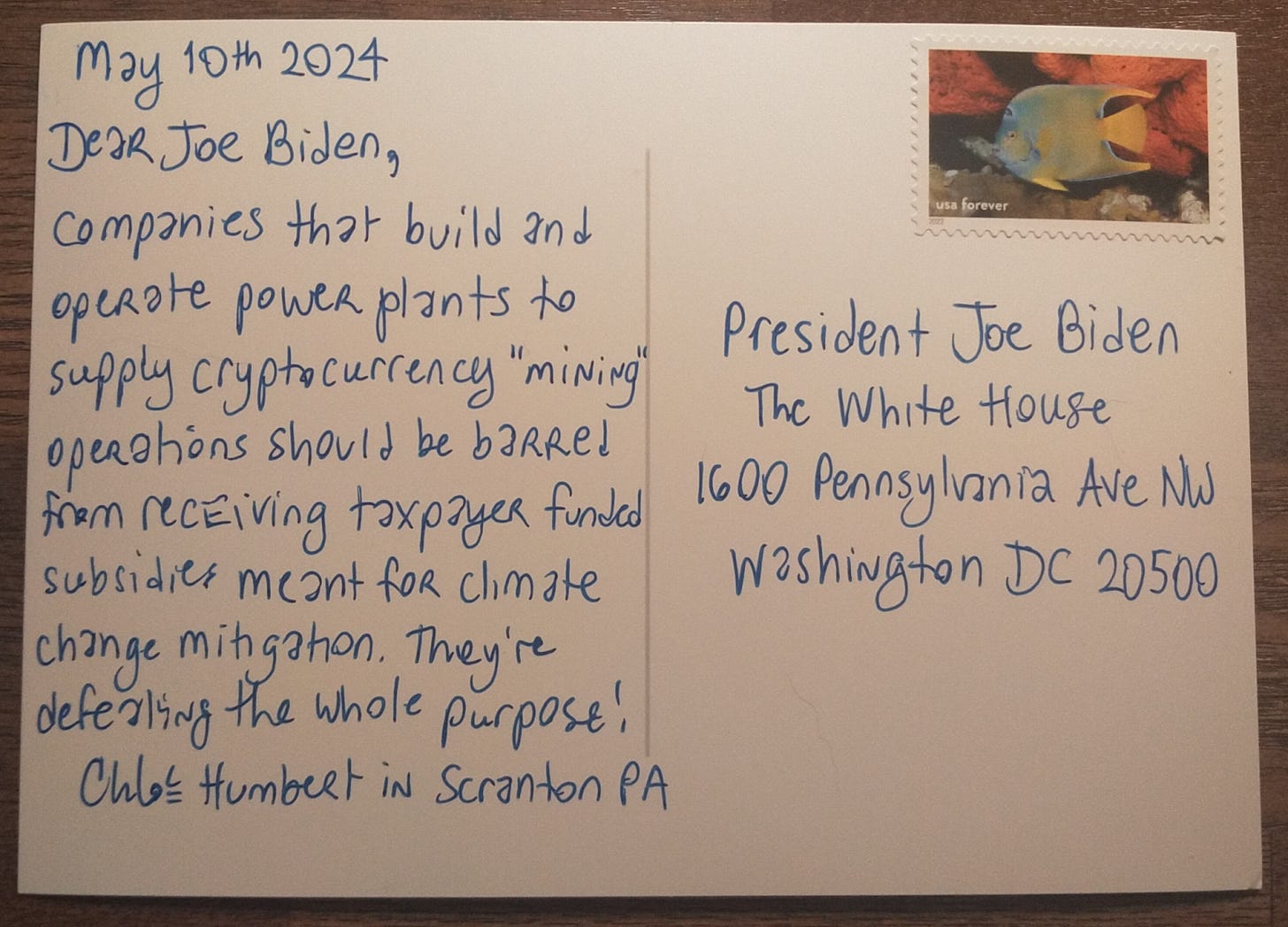 Image is a postcard the text reads: May 10th 2024. Companies that build and operate power plants to supply cryptocurrency “mining” operations should be barred from receiving taxpayer subsidies meant for climate change mitigation. They’re defeating the whole purpose. Chloe Humbert in Scranton PA. Addressed to President Joe Biden at the White House, on a postcard with National Marine Sanctuary stamp with the picture of a tropical fish. 