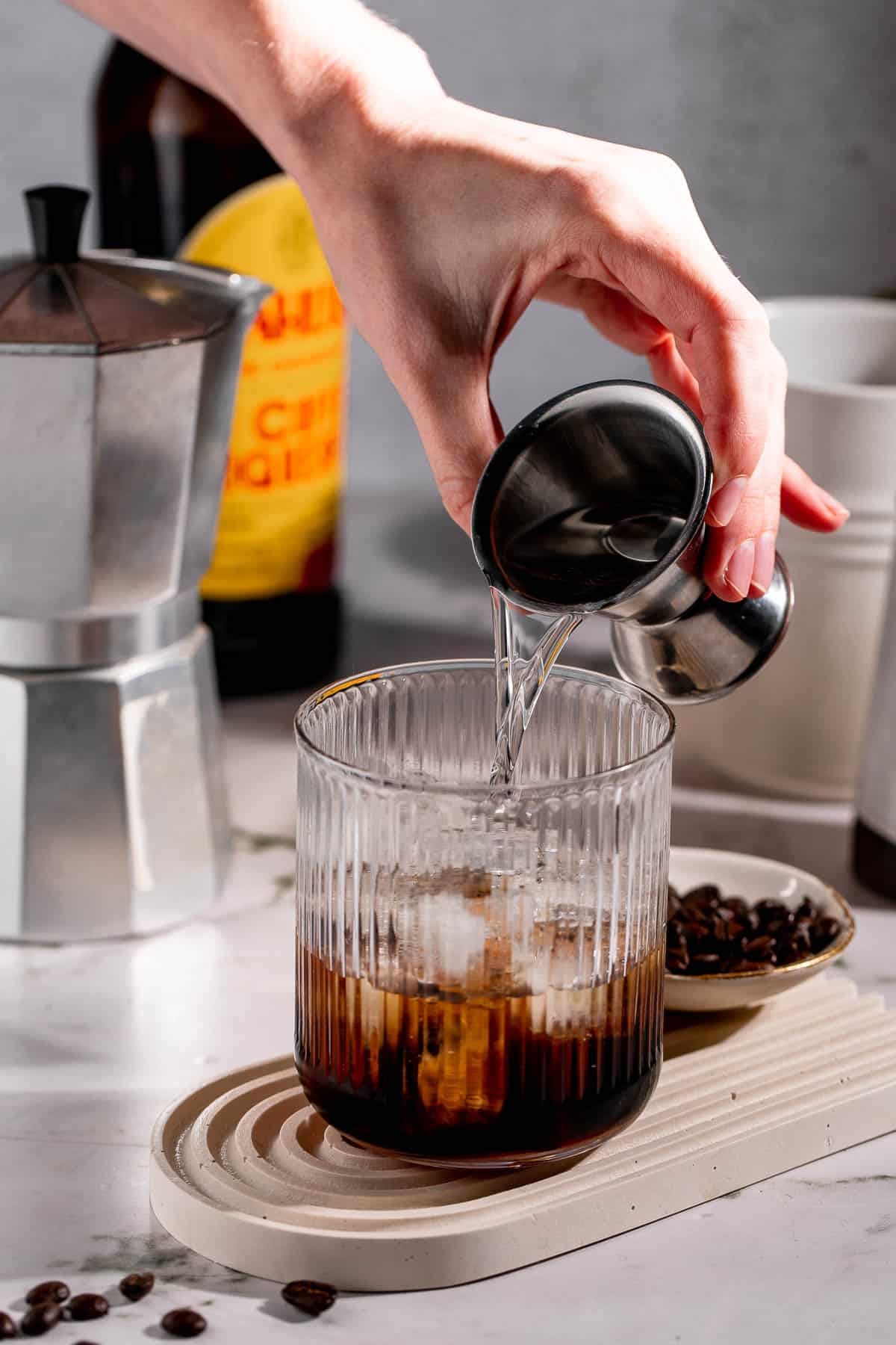 Vodka pouring into a serving glass filled with ice cubes.