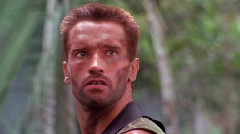 Arnold as Dutch in Predator, looking just over the camera with a confused stare.